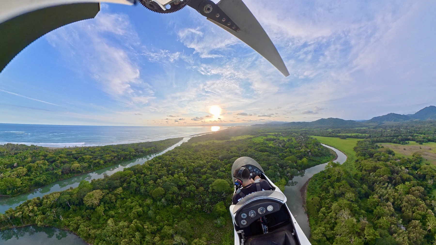 View from a gyrocopter flying over the coast and a winding river at sunset